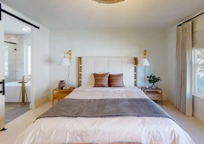 Spacious and serene bedroom design with a large bed, white linens, earth-toned pillows, wall-mounted lamps, and a sliding barn door.