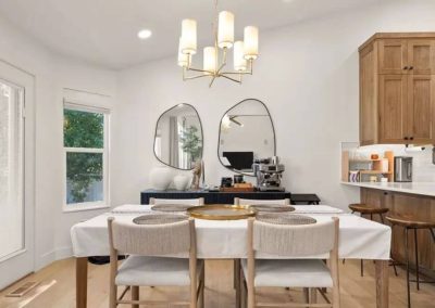 Chic dining space with a white table, textured chairs, twin round mirrors on the wall, and an adjacent kitchen area with a coffee machine on the counter.